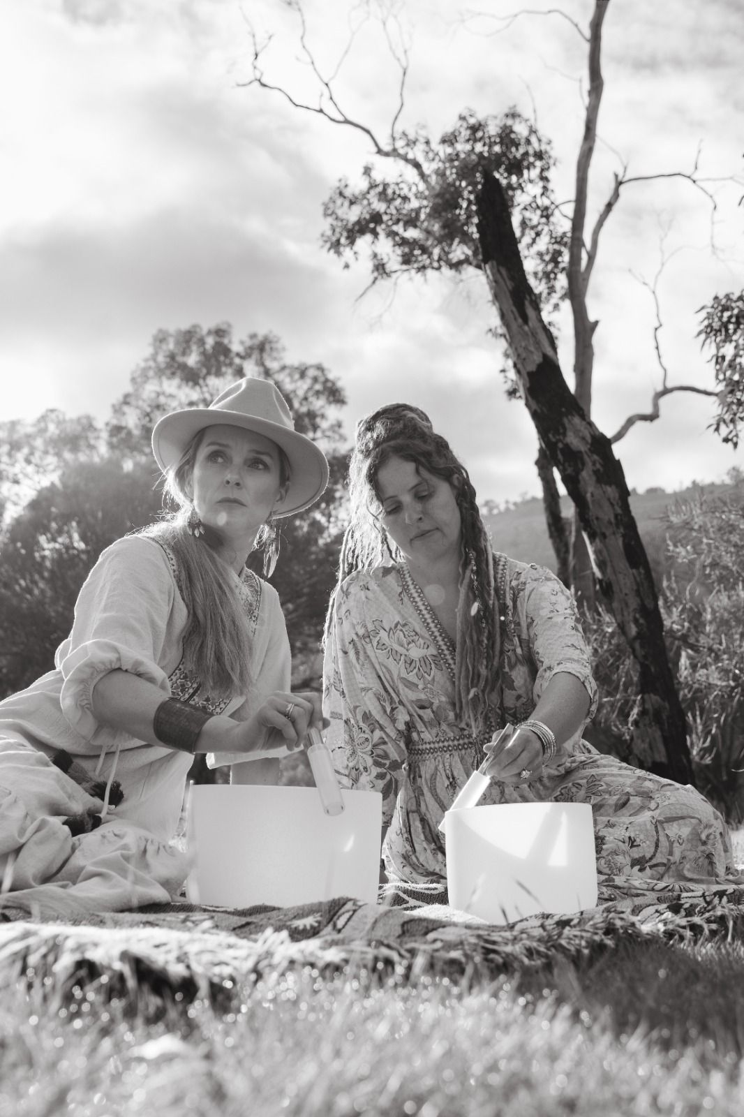 Two women playing crystal singing bowls outdoors
